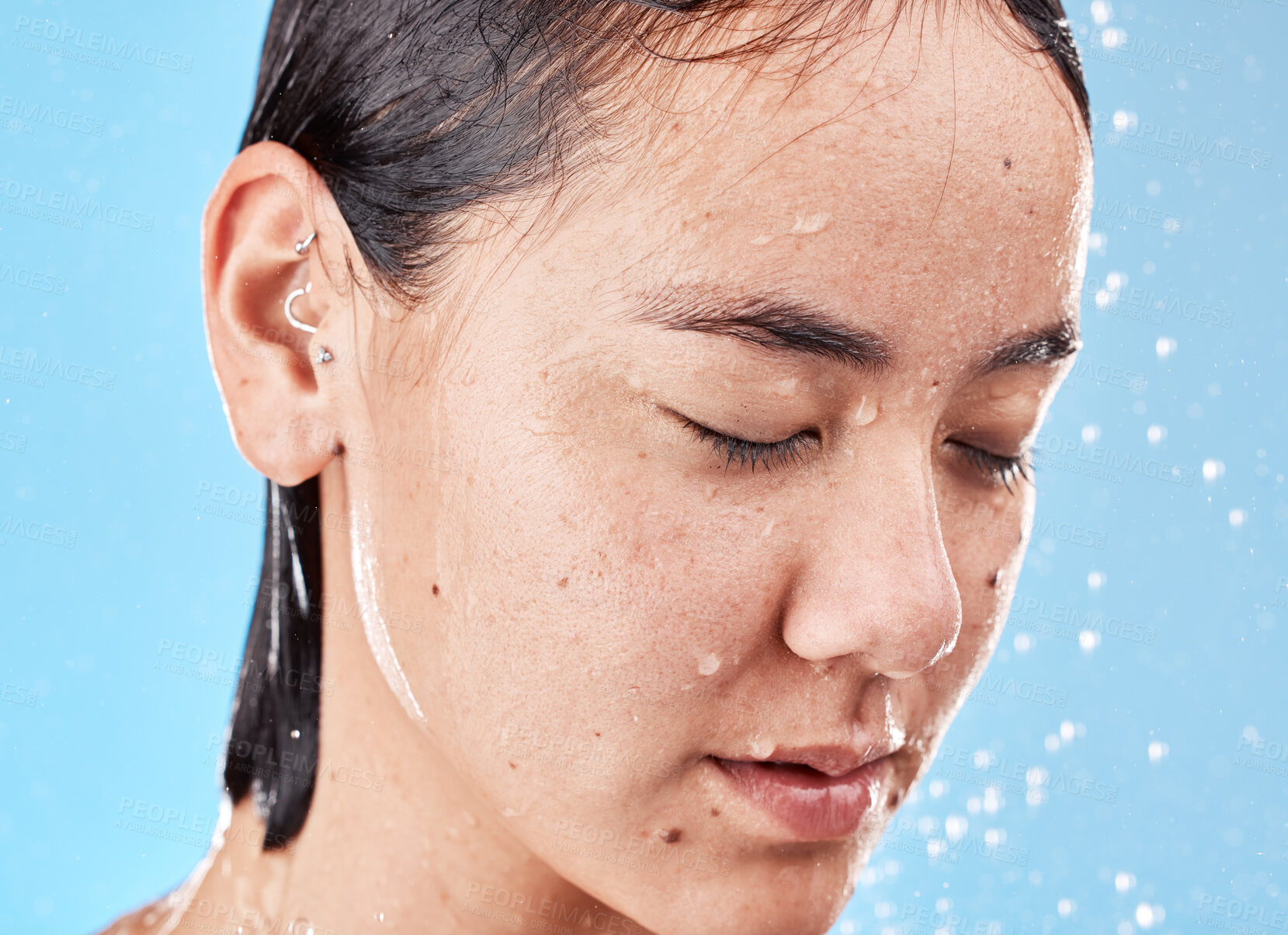 Buy stock photo Calm, water and woman in the shower for grooming, hygiene and relax against a blue studio background. Cleaning, skincare and Asian model relaxing during body care for wellness, beauty and routine