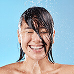 Shower, water and happy woman with smile in studio for skin health, wellness and hygiene. Happiness, beauty and wet Asian model cleaning or washing her body, face and hair isolated by blue background