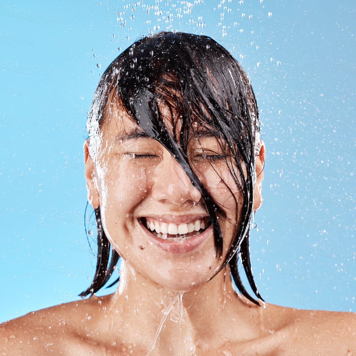 Buy stock photo Shower, water and happy woman with smile in studio for skin health, wellness and hygiene. Happiness, beauty and wet Asian model cleaning or washing her body, face and hair isolated by blue background