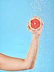 Grapefruit, arm and shower for natural healthcare or skincare cleaning. Luxury fruit, skin beauty and model hand with vitamin c wellness for tropical nutrition under water in blue background studio