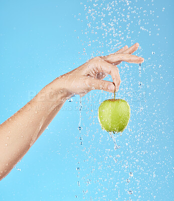 Buy stock photo Water, splash and hand with apple in studio for health, nutrition and wellness. Natural diet, healthy eating and person holding fruit with water splash, drop and stream isolated on blue background