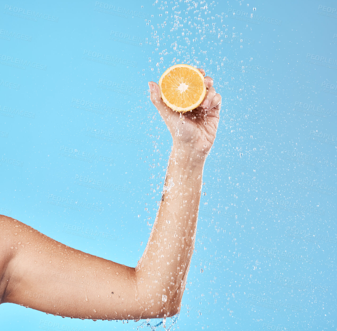 Buy stock photo Hand, orange and water with a woman in studio on a blue background for health or hydration. Food, luxury and wellness with a female holding fruit in the bathroom shower for natural nutrition