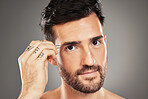 Face, portrait and tweezers with a man model plucking his eyebrows in studio on a gray background. Skincare, wellness and luxury with a handsome young male tweezing his eyebrow hair for grooming