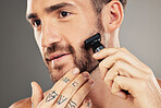 Shaver, beard and man grooming in a studio for beauty, hygiene and skincare for wellness. Health, shave and healthy guy shaving his facial hair with a cosmetic razor isolated by a gray background.