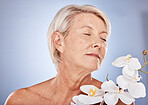 Flowers, skincare and senior woman with aromatherapy, beauty and peace from plants against a grey studio background. Luxury, cosmetic and calm elderly model with an orchid for wellness and relax