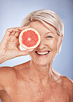 Face portrait, skincare and old woman with grapefruit isolated on a blue studio background. Smile, happy and elderly female model holding fruit for natural vitamin c, facial care and skin wellness.
