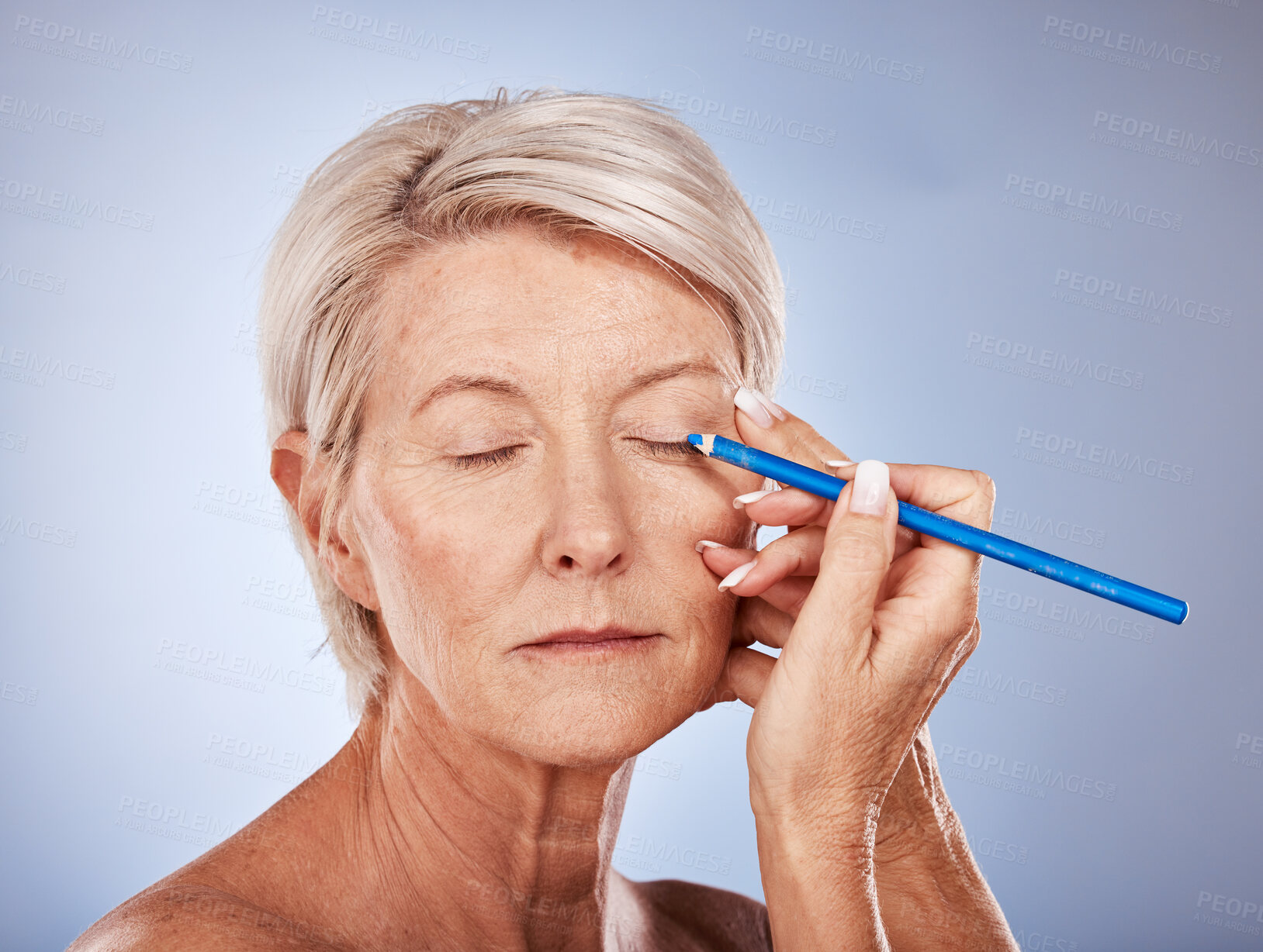 Buy stock photo Makeup, beauty and senior woman with eyeliner for color on face against a grey studio background. Cosmetic, skin and elderly model with a pencil for facial cosmetics, natural art and creativity