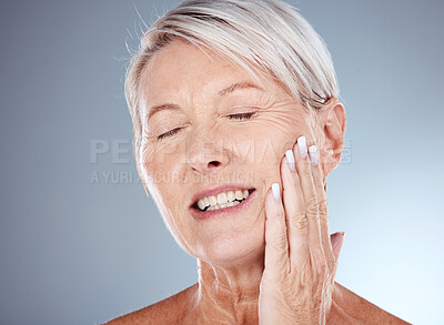 Buy stock photo Elderly woman, hand and smile for skincare, cosmetics or moisturizer against a grey studio background. Senior female touching face and smiling in satisfaction for healthy anti aging facial treatment
