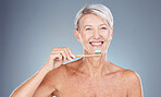 Teeth, dental care and mature woman with toothbrush and toothpaste on gray background with smile on face. Morning routine, healthcare and fresh, happy senior lady in studio portrait cleaning mouth.