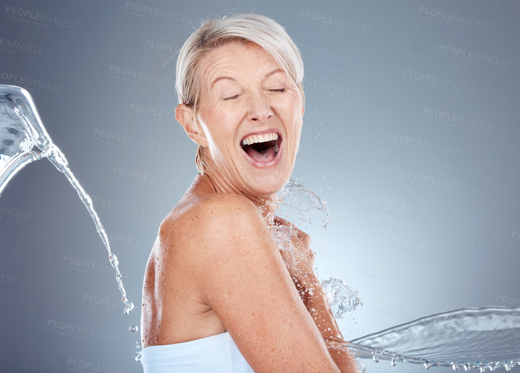 Buy stock photo Water splash, health and portrait of senior woman shocked and surprised on gray background. Skincare, wellness and beauty, a happy mature lady splashed with water with happy smile on face in studio.