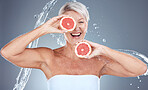 Grapefruit, water and senior woman with a splash for skincare, beauty and wellness against a grey studio background. Water splash, health and excited elderly model with fruit for diet lifestyle
