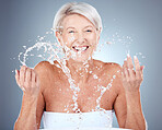 Mature woman, water and splash for beauty, skincare and hygiene or grooming on a grey studio background. Senior woman, fresh and facial wash or cleansing for healthy skin and wellness portrait