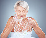 Water, splash and senior woman in studio for natural, cosmetic and facial routine for hygiene. Health, wellness and elderly lady doing clean, organic and beauty skincare treatment by gray background.