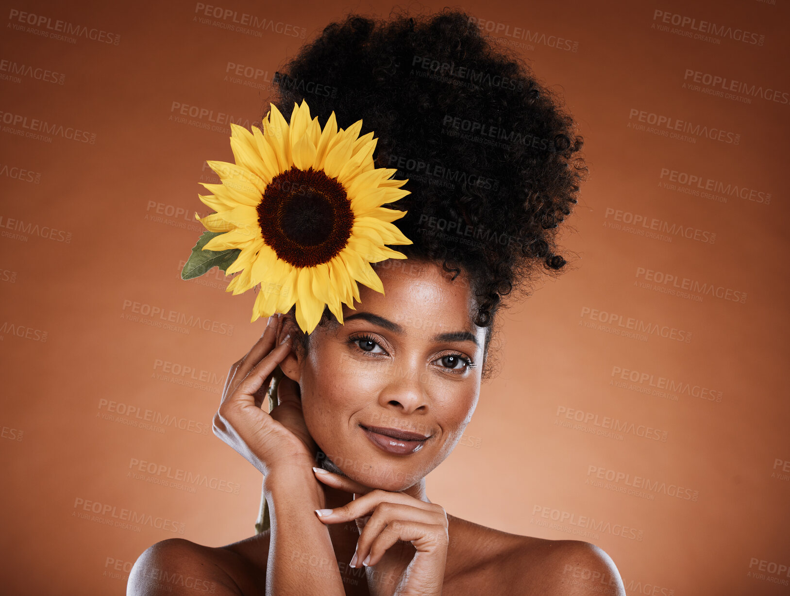 Buy stock photo Black woman, beauty and flower for organic cosmetics for aesthetic health and wellness on a brown studio background. Makeup, sunflower and african american female with a clean face for skincare