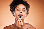 Lipstick, black woman and cosmetics for smooth, glow and skincare with confidence with brown studio background.  Lips, African American female and girl with gloss, makeup and natural beauty for mouth