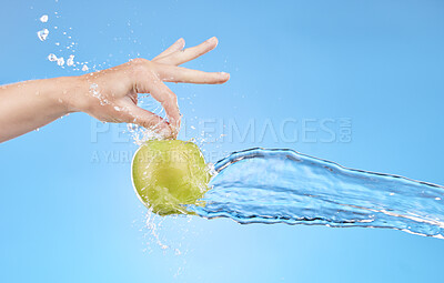 Buy stock photo Hand, water and apple in studio on a blue background for health, diet or wellness. Food, splash and nutrition with a green fruit in the hands of a woman for vitamins, nutrition or hydration