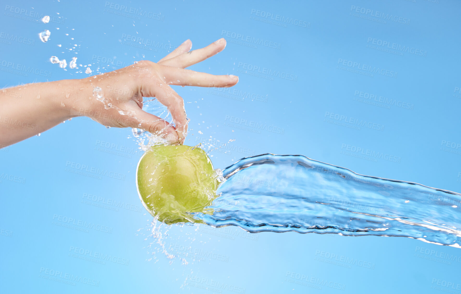 Buy stock photo Hand, water and apple in studio on a blue background for health, diet or wellness. Food, splash and nutrition with a green fruit in the hands of a woman for vitamins, nutrition or hydration