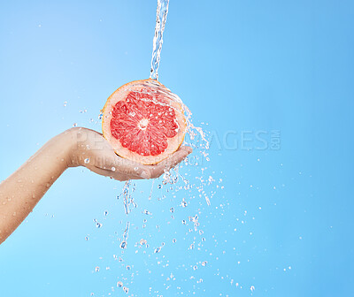 Buy stock photo Hand, grapefruit and water splash for skincare nutrition, wellness or cosmetics against a blue studio background. Person hold citrus fruit in healthy, hydration or hygiene for natural vitamin C skin