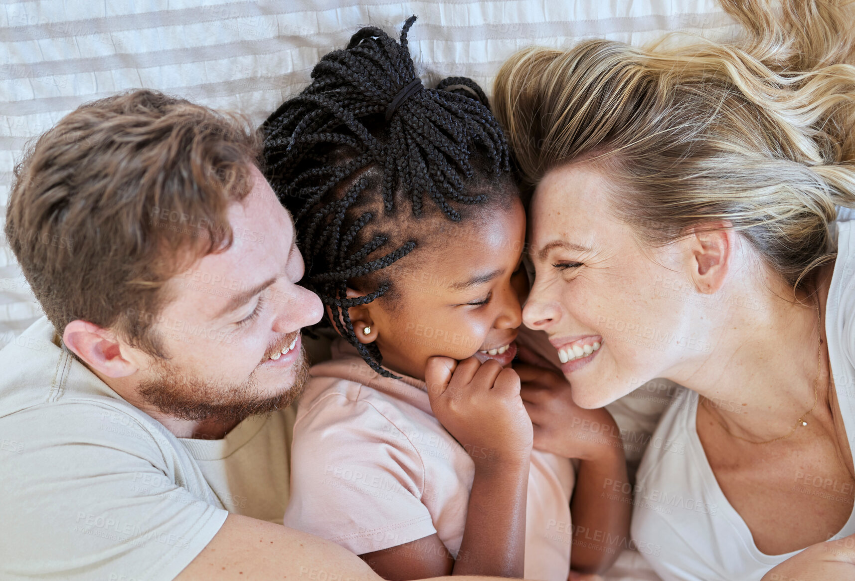 Buy stock photo Family, interracial and love, happy and together with adoption or foster care overhead and bonding together in family home. Happy family lying on bed, cuddle and smile with mother, father and child.
