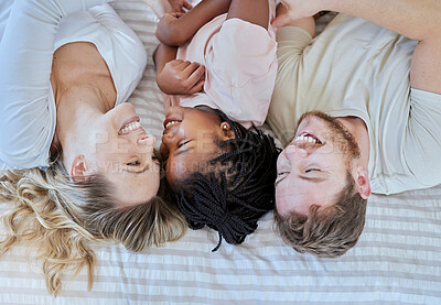Buy stock photo Family, love and happy together with care in family home, smile in overhead with adoption or foster care. Happy family, interracial and happiness with mother, father and child lying on bed bonding.