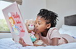 Reading, book and teddy bear with a black girl in bed, lying down to relax in the bedroom with her hobby. Children, books and education with a female kid telling her teddybear a story in their home