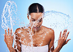 Water splash, skincare and woman cleaning face in studio isolated on blue background. Health, wellness or hygiene of female model from India washing and bathing for beauty, body care and healthy skin