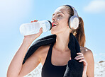 Woman, drink and water bottle during fitness, run outdoor with towel and music with headphones or streaming podcast for exercise motivation. Hydration, wellness and drinking water after workout.