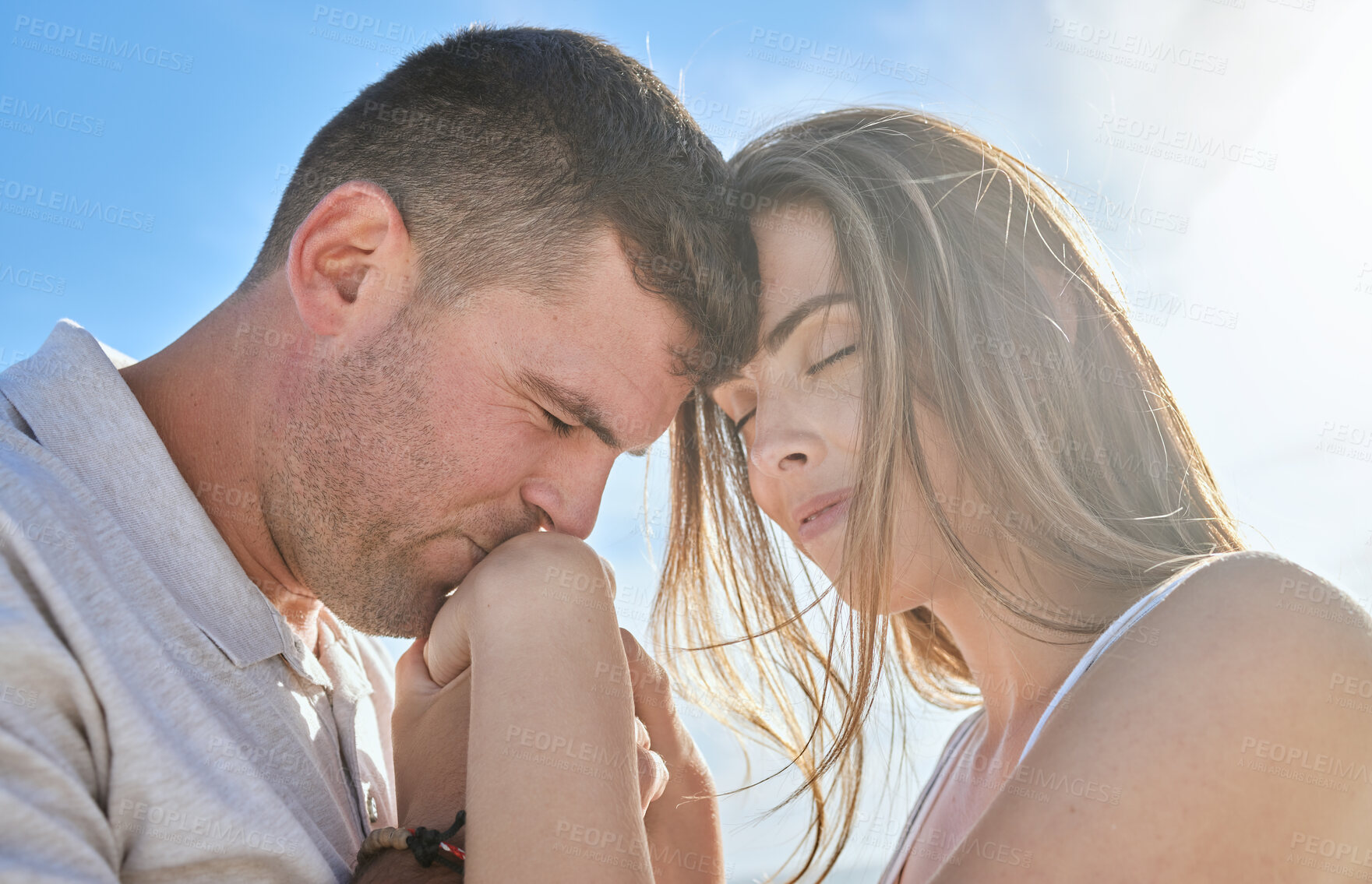 Buy stock photo Love, hand and couple kiss at a beach, sharing intimate moment of romance at sunrise against blue sky background. Travel, freedom and man with woman embrace, care and relax in nature together mockup