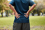 Exercise, fitness and back pain of man at park after workout. Break, healthcare or mature male runner with back injury, muscle pain and inflammation after exercising, running or training in nature


