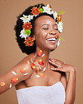 Black woman, happy and flowers in studio for wellness, pamper and nature product against brown background. Smile, girl model and flower, crown and cosmetics for beauty, zen and aesthetic with mockup