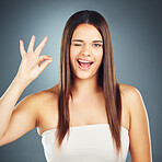 Hand sign, perfect and wink with a model woman in studio on a blue background for skin or hair care. Portrait, face and solan with an attractive young female using a gesture to show satisfaction