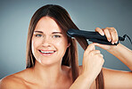 Beauty, hair care and flat iron with a model woman in studio on a gray background to straighten her hair. Wellness, growth and straight with an attractive young female using a hair straightener