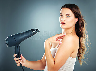 Buy stock photo Beauty, haircare and hairdryer with a model woman in studio on a blue background drying her hair with an appliance. Wellness, salon and luxury with an attractive young female blowdrying her hairstyle