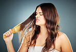 Hair care, brush and frustrated woman brushing damaged and tangled hair on a gradient studio background. Female model with crisis, stress and disaster with hair loss problem with hairdresser shampoo