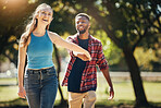 Love, garden and happy couple holding hands while walking together on a date in a green park. Happiness, love and interracial young man and woman bonding while on a walk in nature for fresh air.