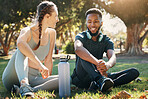 Couple, exercise and relax on grass in nature park for fitness rest, water hydration and interracial health discussion. Diversity, friends conversation and healthy cardio training break together