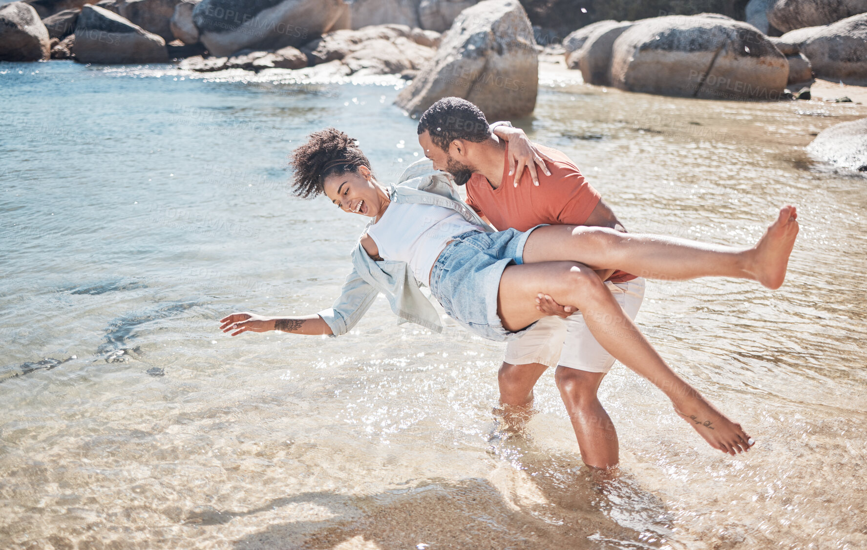 Buy stock photo Couple, love and man carrying woman on beach for funny, comic or relax travel adventure together. Happiness, support and african person carry wife, quality time in water for Hawaii summer vacation