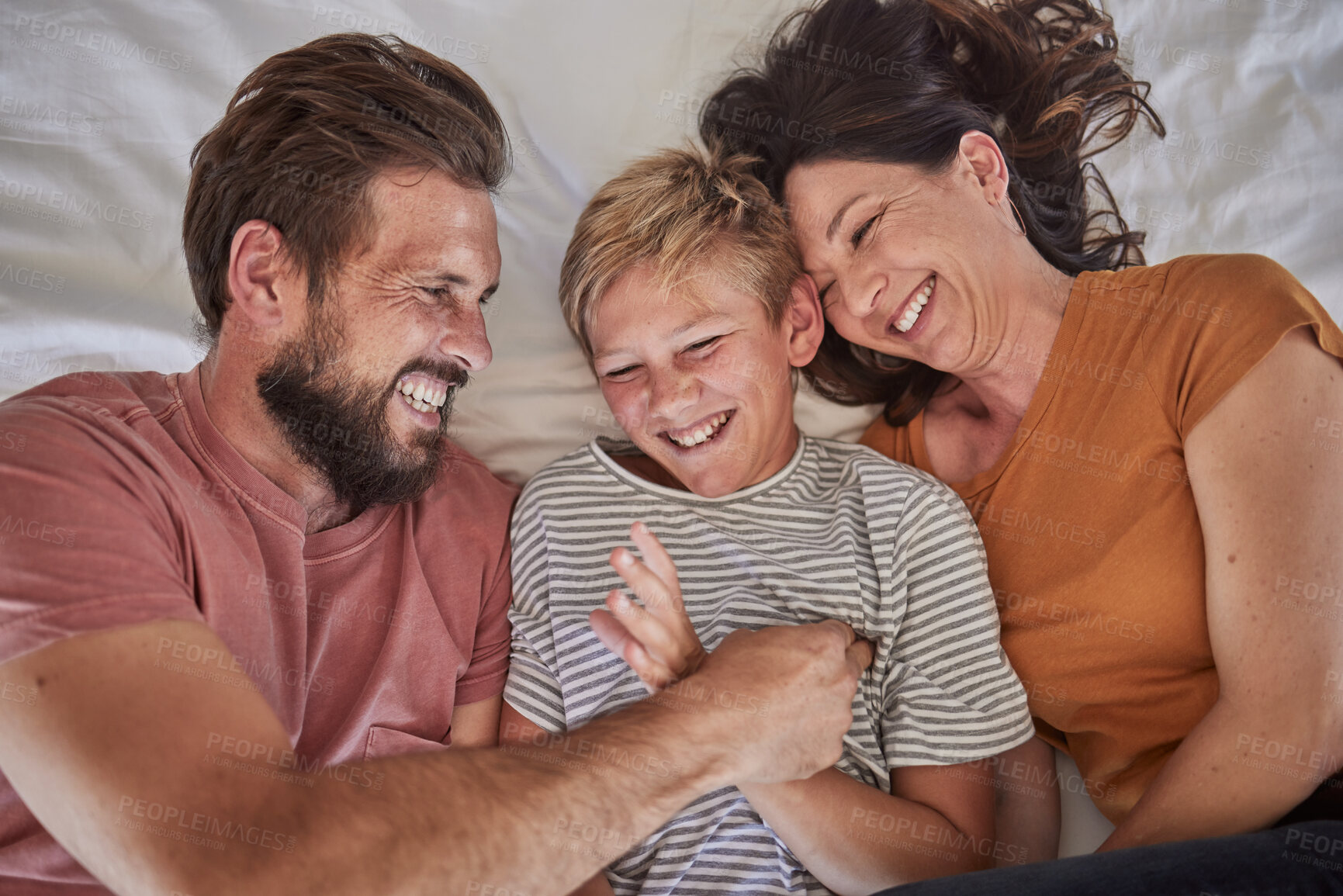 Buy stock photo Top view, parents or boy bonding in tickle game on house, family home or hotel bed in trust, love or security. Smile, happy man or laughing woman and son, comic child or preteen kid in funny activity