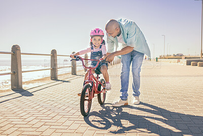 Buy stock photo Father, child and bicycle with a girl learning to ride a bike on promenade by sea for fun, bonding and quality time on summer vacation. Man teaching his daughter or girl safety while cycling outdoor