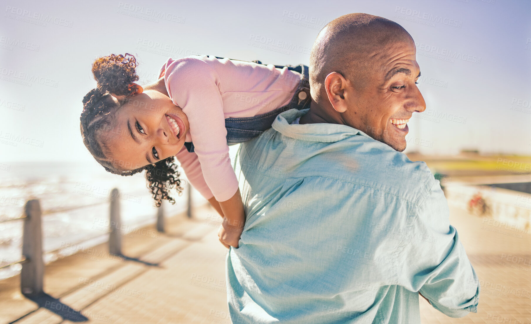 Buy stock photo Family, love and father carrying girl, playing or bonding outdoors by promenade. Support, care or portrait of man with child, daughter or kid, enjoying quality time together or having fun by seashore