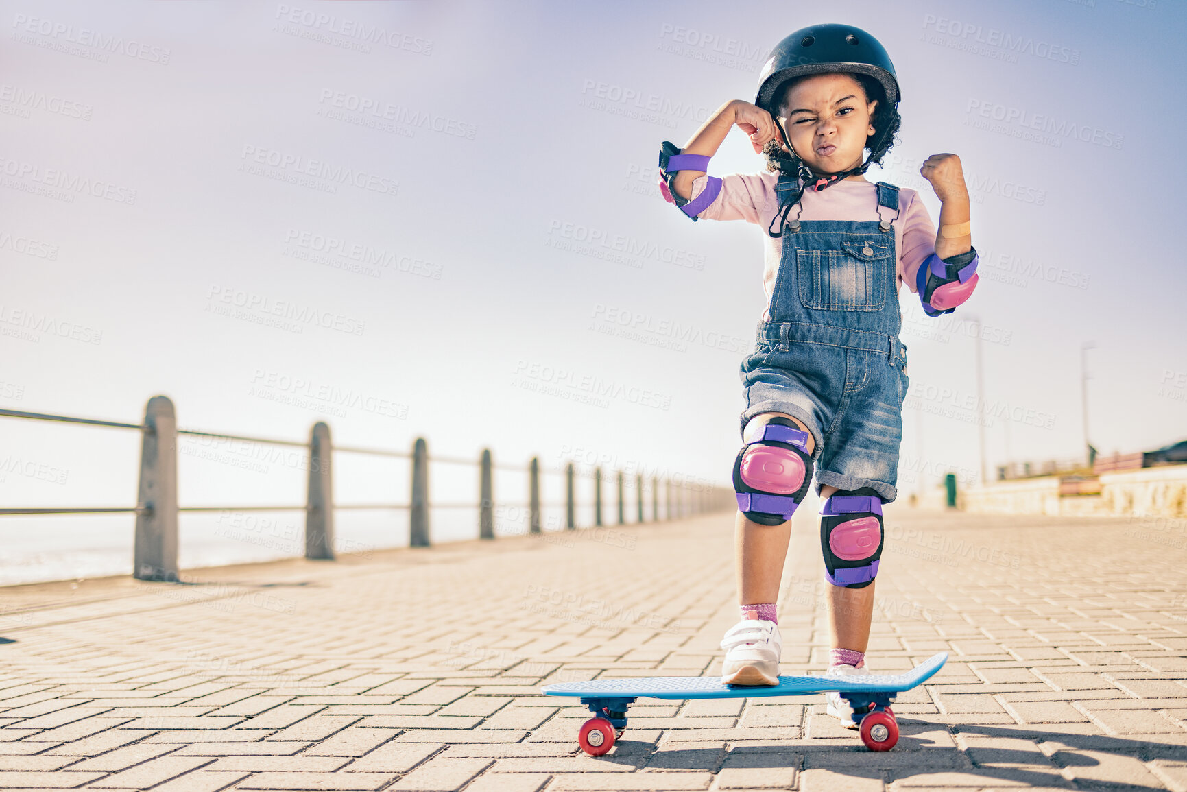 Buy stock photo Children, skate and strong with a girl on her skateboard for fun on the beach promenade alone during summer. Muscle, bicep and helmet with a female child skating outside on a sidewalk with knee pads