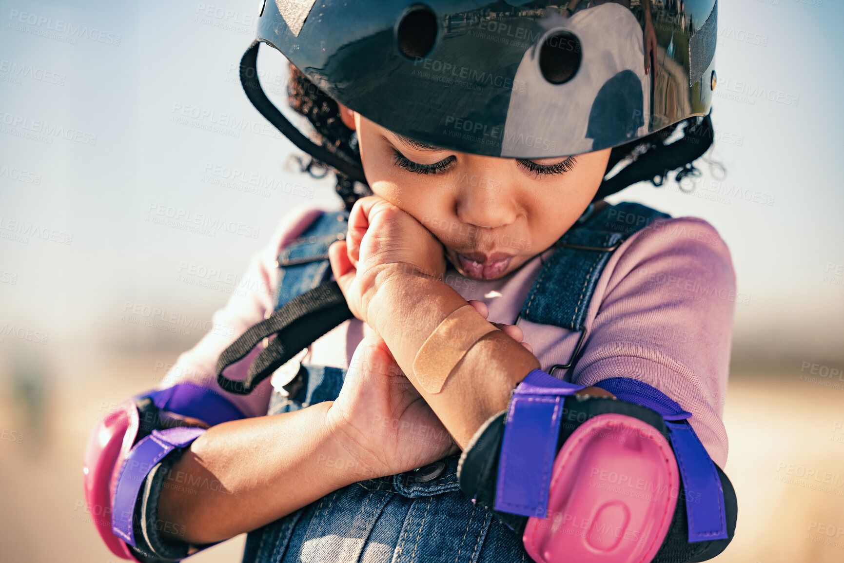 Buy stock photo Children, skater and plaster with an injured girl looking at her sore arm while skating outdoor in a helmet and pads. Training, safety and injury with a female kid in pain after a sports accident