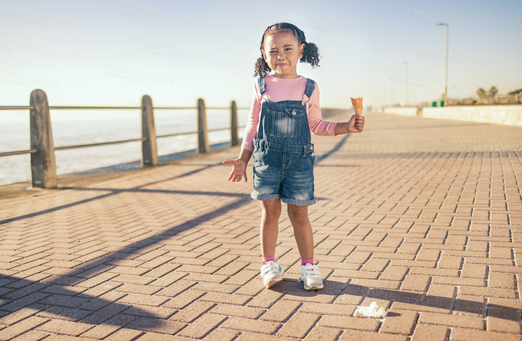 Buy stock photo Upset little girl, ice cream and sad in Cape Town with expression in frustration for a spoilt day by the ocean bay. Unhappy moody child holding empty icecream cone melting mess on floor at sea point