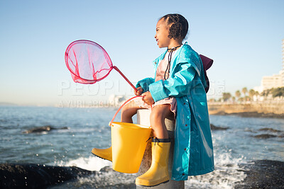 Buy stock photo Girl, beach and fishing net with bucket, water and rock pool for outdoor adventure with boots, smile and ocean. Black child, sea and happy for fish, waves or sea in nature, learning and sunshine