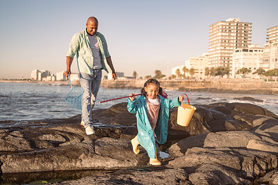 Buy stock photo Father, girl and fishing at beach, learning and happy together outdoor in summer, bonding or fun on rocks. Black man teaching kid to catch fish, rod and bucket with family at a ocean, sea  and nature