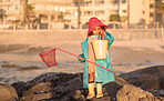 Beach, fishing and girl with a net and bucket standing on a rock by the ocean on vacation. Outdoor, nature and child at the seaside to catch fish in the sea water for an adventure while on holiday. 