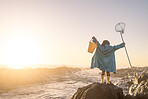 Child, freedom and fishing at sunset while at beach excited, happy and waiting for ocean waves outdoor while on vacation. Girl on a rock with a bucket and net to catch fish and have fun on holiday