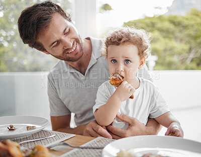 Buy stock photo Father, baby and eating at lunch table for bonding together in family home with hungry child. Food, health and wellness of independent and cute kid eating chicken with proud smile of dad.


