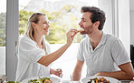 Couple, food and eating lunch with a woman feeding her man on a romantic date at home at the dining table. Health, nutrition and diet with a husband and wife eating delicious meal or lunch
