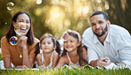Bubbles, family and relax on grass at park, nature or outdoors on summer vacation. Happy portrait, smile and care of parents and girls bonding, enjoying quality time together and having fun in garden